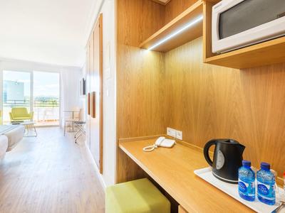 Chambre d'hôtel lumineuse avec bureau en bois, bouteilles d'eau, bouilloire et vue sur la fenêtre.