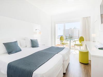 Helles Hotelzimmer mit zwei Einzelbetten, blau-weißer Bettwäsche, Balkon und moderne Möbel in Weiß und Grün.