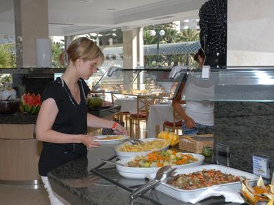Femme se sert au buffet avec divers plats dans un restaurant d'hôtel élégant.