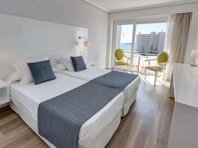 Chambre d'hôtel moderne avec deux lits simples, cache-lits gris et balcon avec vue sur la ville.