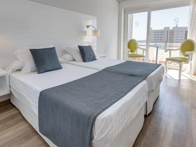 Chambre d'hôtel moderne avec deux lits simples, jetés de lit gris et chaises près de la fenêtre du balcon.