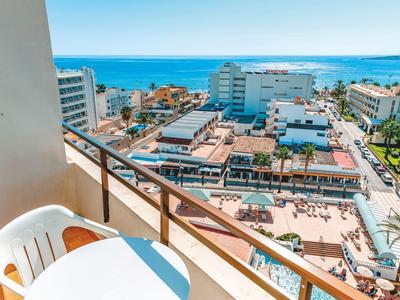 Balcon avec chaise et table surplombant la ville et la mer sous un ciel clair.