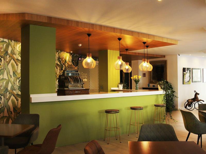 Espace bar d'hôtel moderne avec comptoir vert, tabourets et éclairage chaleureux.
