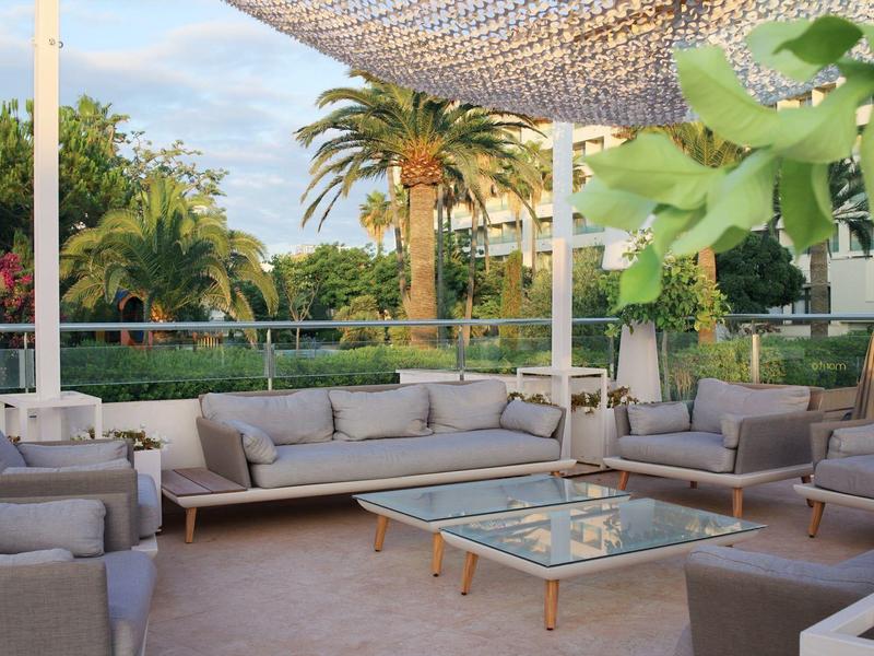 Espace salon extérieur confortable sous ombrage avec des palmiers en arrière-plan.