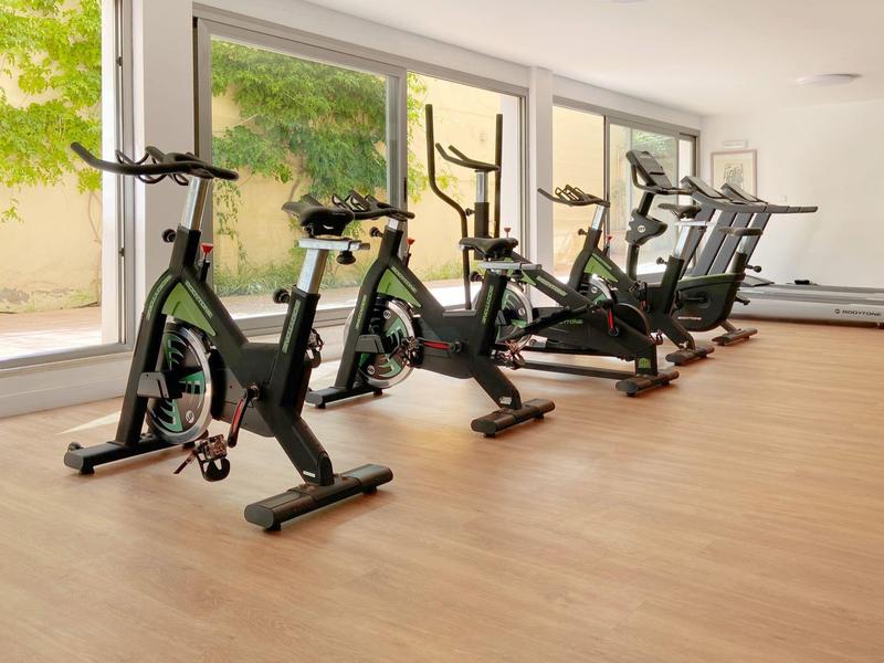 Salle de sport moderne avec vélos de spinning et tapis de course devant de grandes fenêtres.