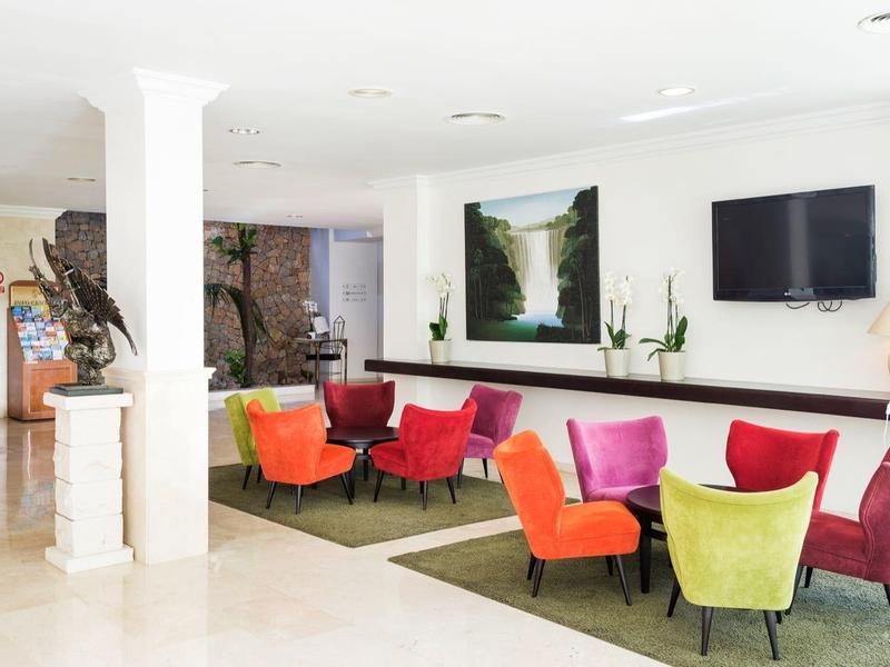 Hall d'hôtel moderne avec fauteuils colorés et télévision sur le mur blanc.