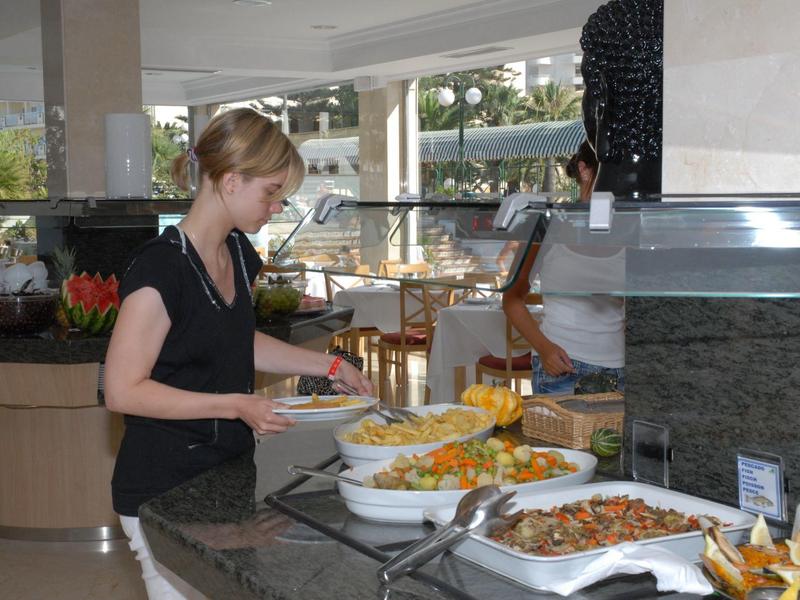 Femme se sert au buffet avec divers plats dans un restaurant d'hôtel élégant.