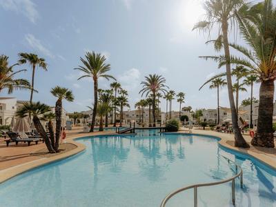 Großer blauer Pool mit Palmen, Liegestühlen und Sonnenschirmen unter klarem Himmel.