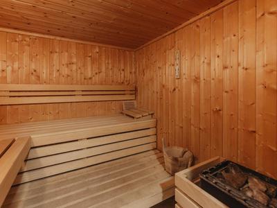 Innenraum einer Sauna mit Holzbänken, Holzwänden und einem Ofen mit Steinen.