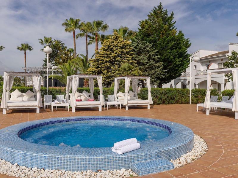 Kruhový bazén s ručníky a bílými baldachýny na terase s palmami.