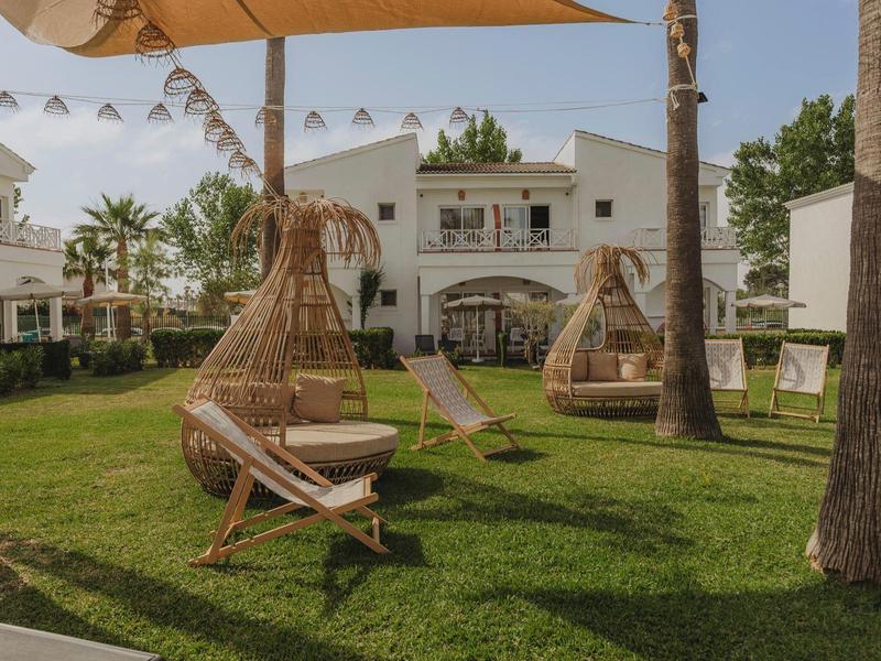 Středomořská venkovní plocha s houpacími křesly a lehátky na zelené trávě.