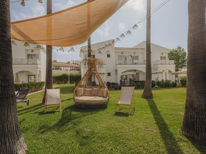 Pohodlné závěsné křeslo a lehátka na zeleném trávníku před hotelem.