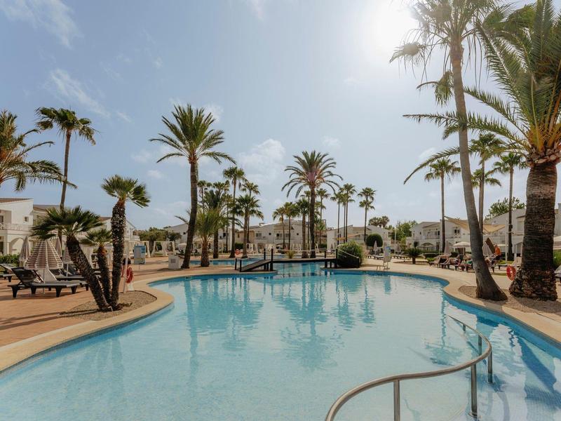 Velký venkovní bazén s palmami a lehátky pod čistou oblohou.