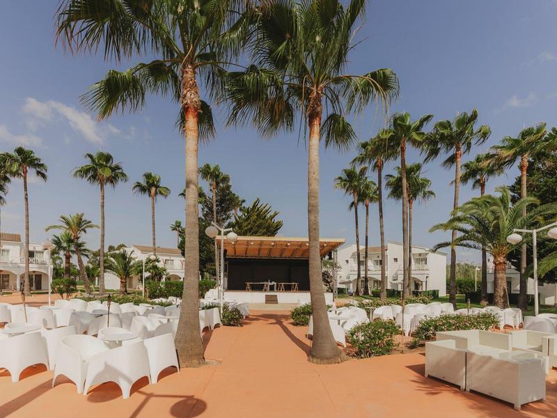 Venkovní prostor s bílými židlemi a palmami pro hotelovou akci za slunečného počasí.