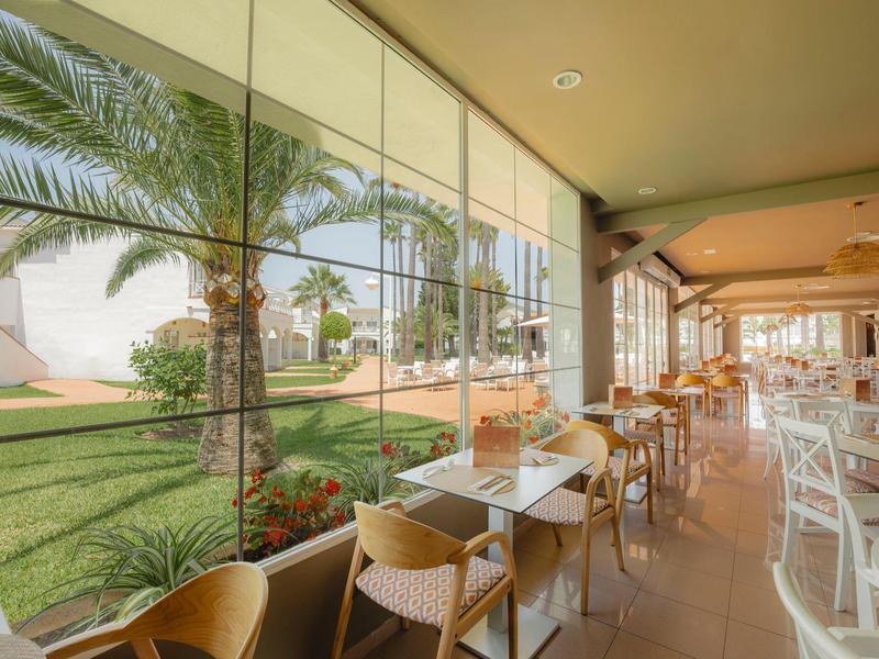 Moderní jídelna se skleněnou zdí s výhledem na zahradu s palmami.