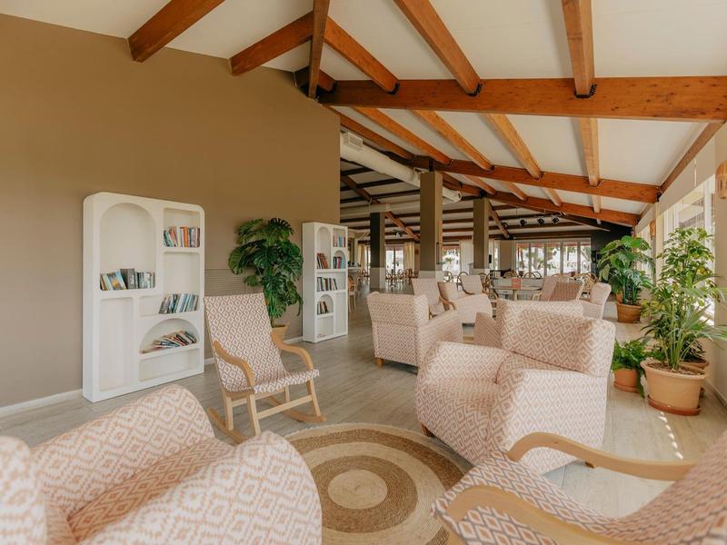 Světlý společenský prostor s pohodlnými křesly, regály a rostlinami.