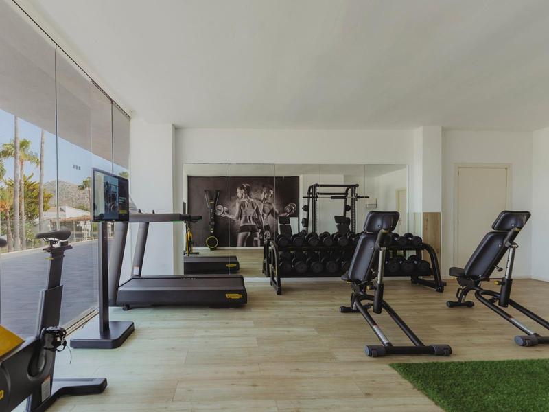 Moderní posilovna s vybavením jako běžecké pásy a závaží u velkých oken.