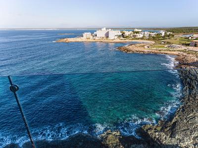 Küstenlinie mit klarem blauem Wasser, Felsen und weißen Gebäuden am Horizont unter blauem Himmel