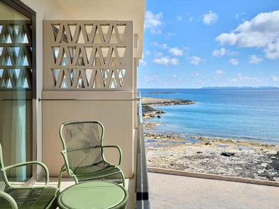 Balkon mit grünem Metallmobiliar und Blick auf felsige Küste und ruhiges blaues Meer.