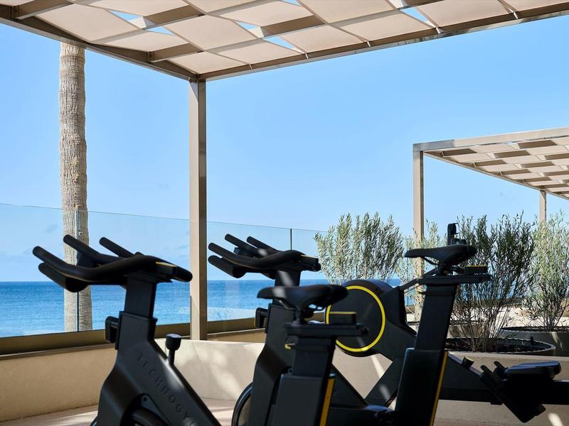 Mehrere Fitness-Fahrräder stehen unter einem überdachten Außenbereich mit Blick auf das Meer.