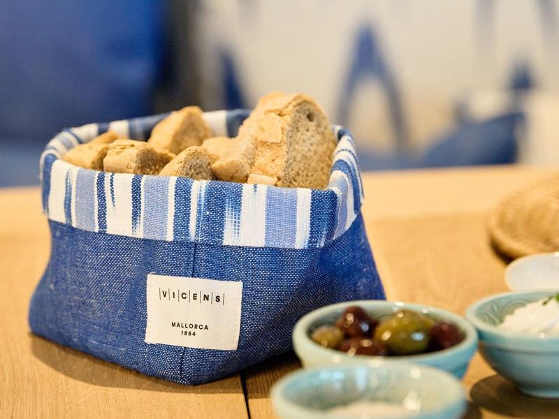 Stoffkorb mit Brotstücken, daneben Schalen mit Oliven und Dips auf Holztisch.