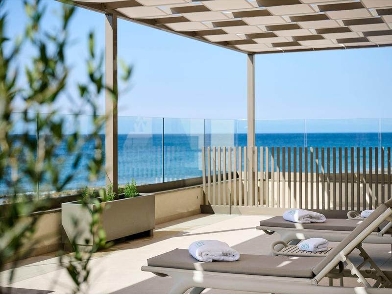 Terrasse mit Liegen, weißen Handtüchern, Sicht auf Meer und blauen Himmel, moderne Pergola.