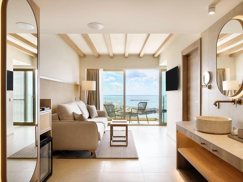 Helles Wohnzimmer mit hellbraunem Sofa, großem Fenster, Balkon und Badezimmer mit Waschbecken und Spiegel.