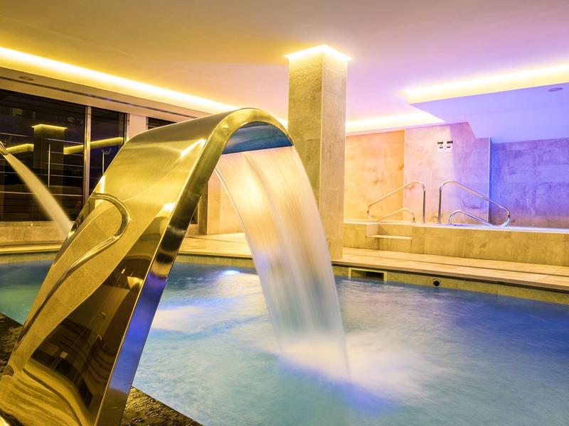 Moderner Innenpool mit Wasserfall und entspannter Beleuchtung in einem Spa-Bereich.