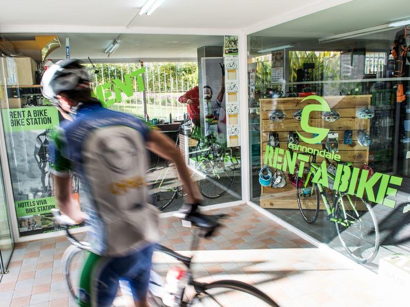 Radfahrer mit Helm und Rucksack fährt an einem Fahrradverleih vorbei.