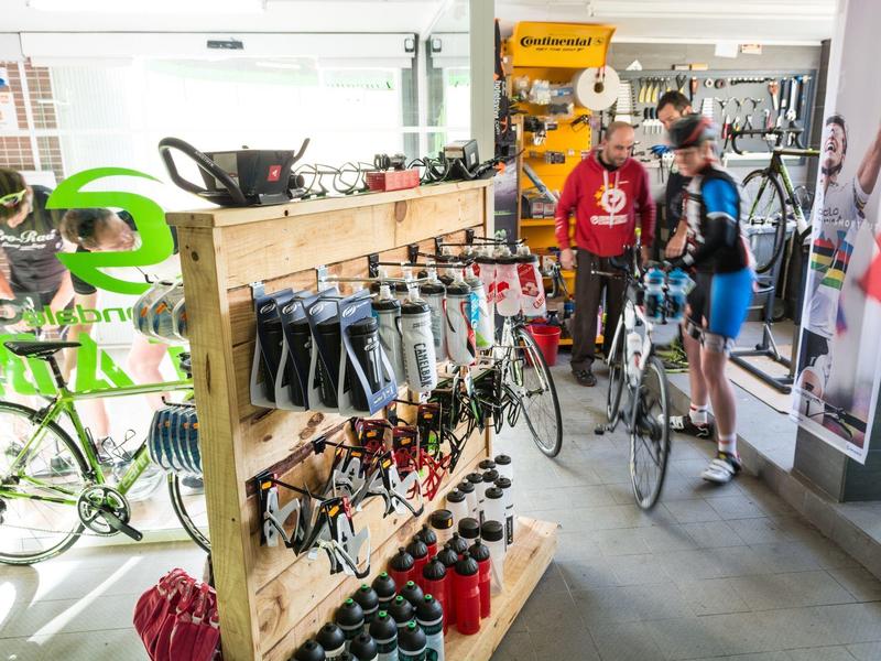 Innenaufnahme eines Fahrradgeschäfts mit Regalen voller Zubehör und Menschen, die Fahrräder betrachten.