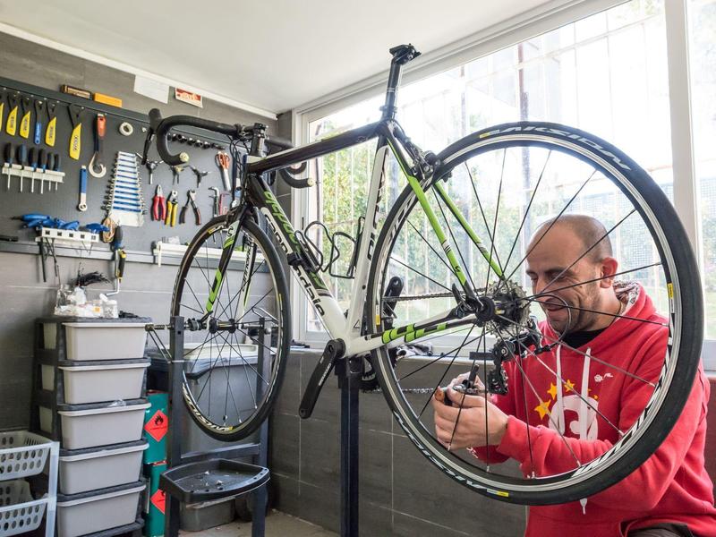 Ein Mann repariert ein Fahrrad in einer Werkstatt mit vielen Werkzeugen und Aufbewahrungsboxen.