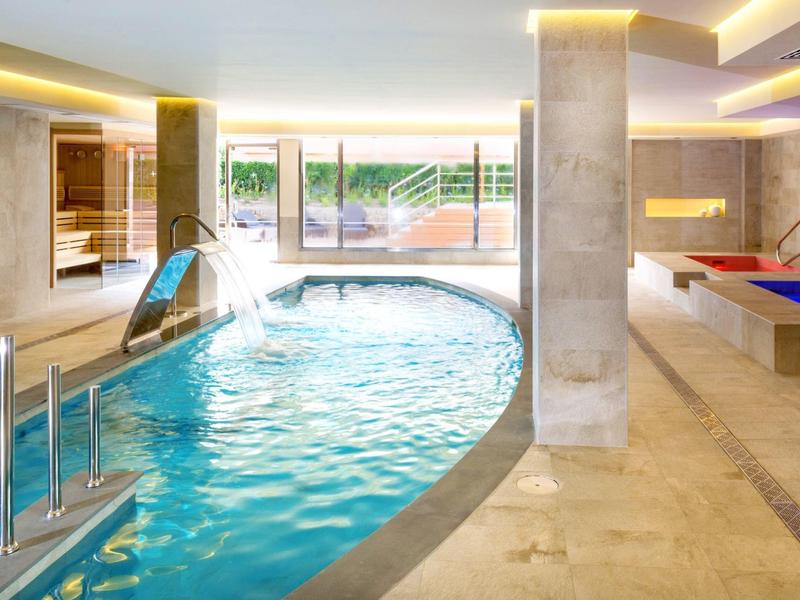 Innenpool mit Wasserrutsche, Sauna und Liegeflächen in einem modernen Wellnessbereich.
