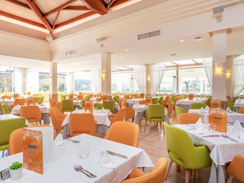 Helles Restaurant mit weißen Tischdecken und bunten Stühlen unter einem Holzdeckenstuhl.