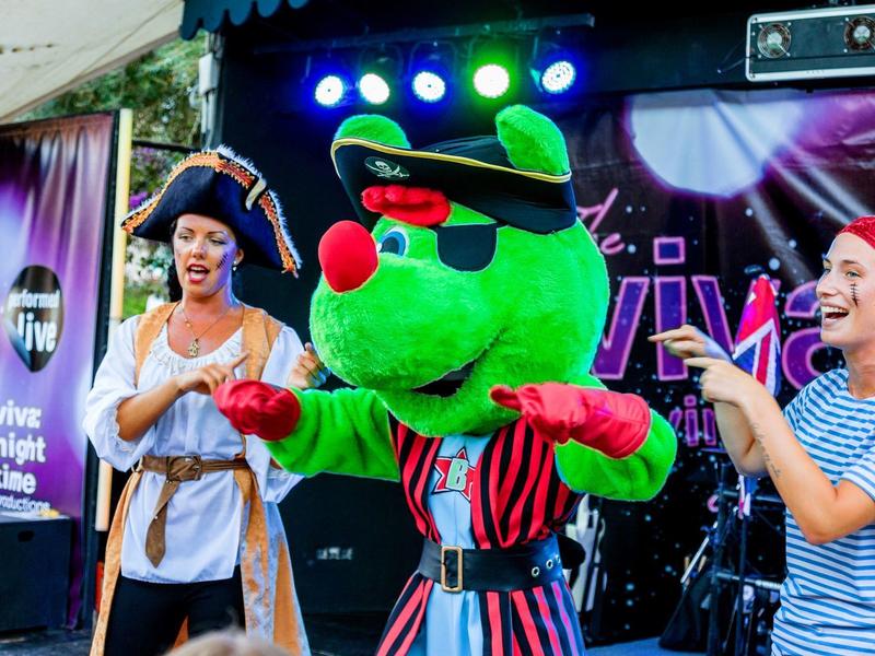 Personen in Kostümen am Abend mit Bühne und bunten Lichtern im Hintergrund
