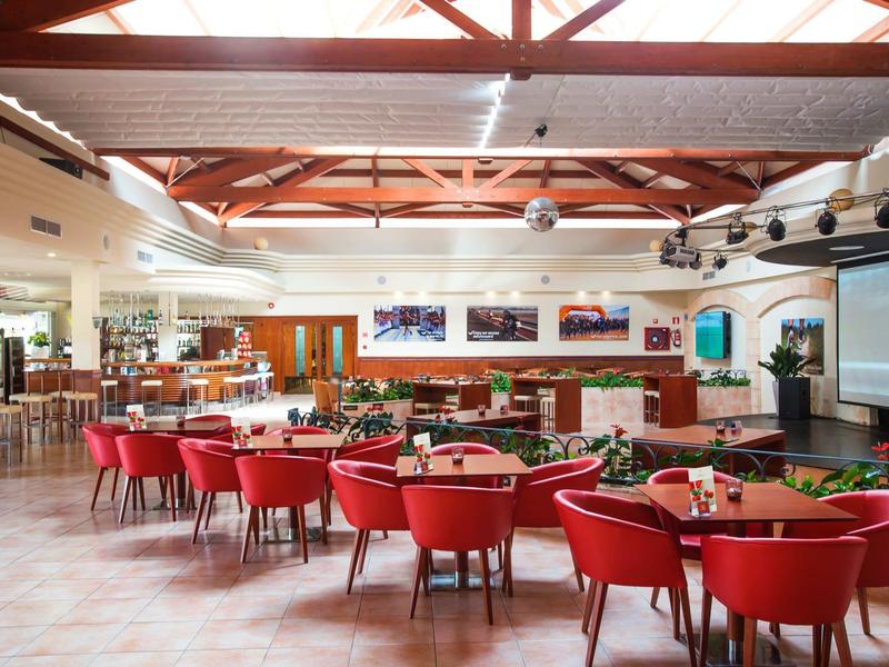 Großer, heller Speisesaal mit roten Stühlen und Holzbalken an der Decke.