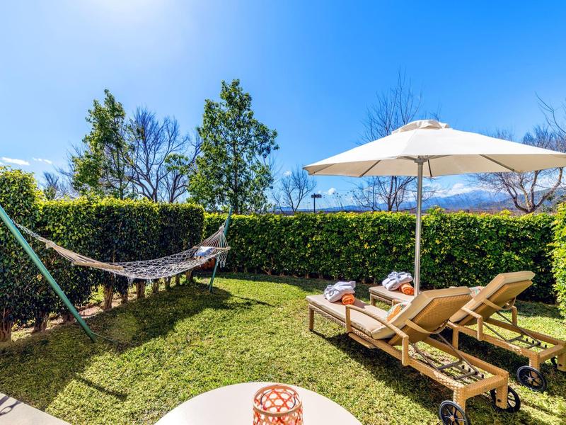 Garten mit zwei Liegestühlen unter Sonnenschirmen und einer Hängematte auf Grasfläche.