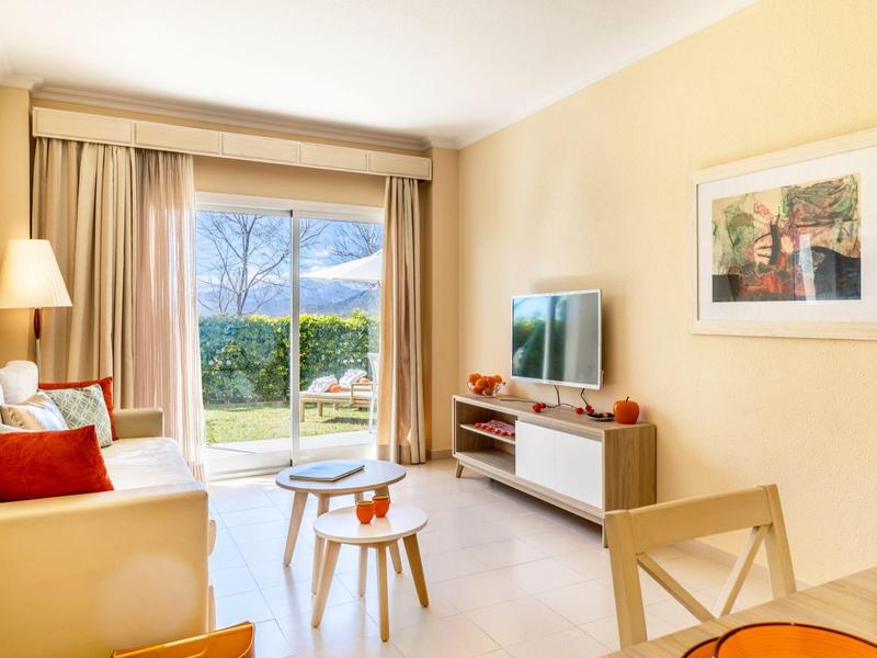 Helles Wohnzimmer mit Sofa, Fernseher und Blick auf Terrasse und Garten.