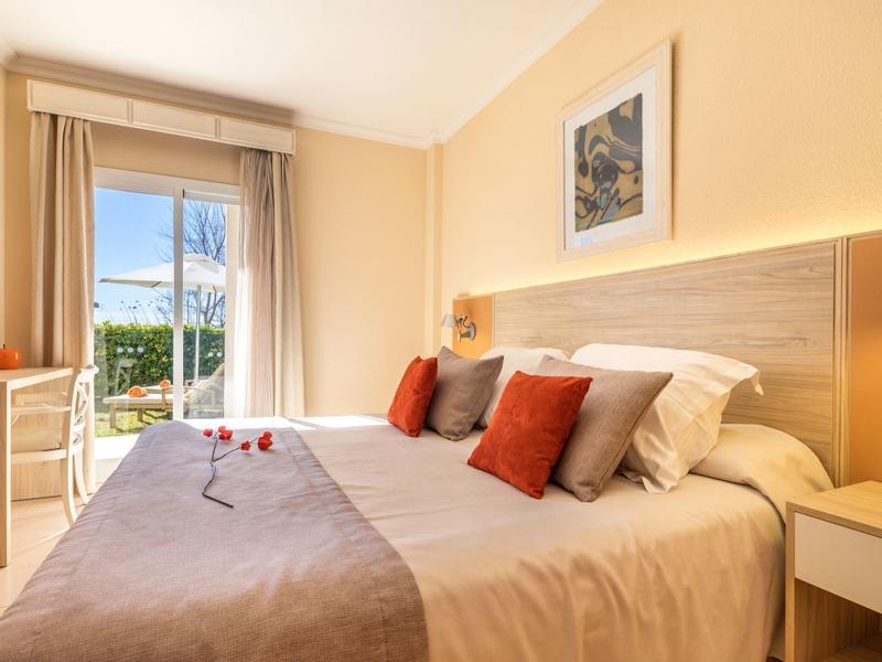 Gemütliches Doppelzimmer mit Terrasse, hellen Wänden und roten Akzentkissen.