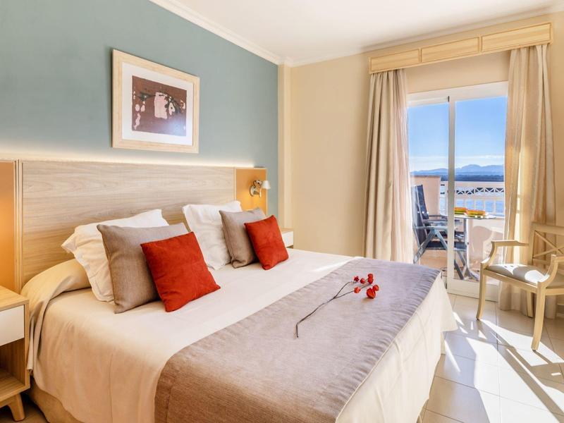 Helles Hotelzimmer mit Doppelbett, Balkon und Meerblick.