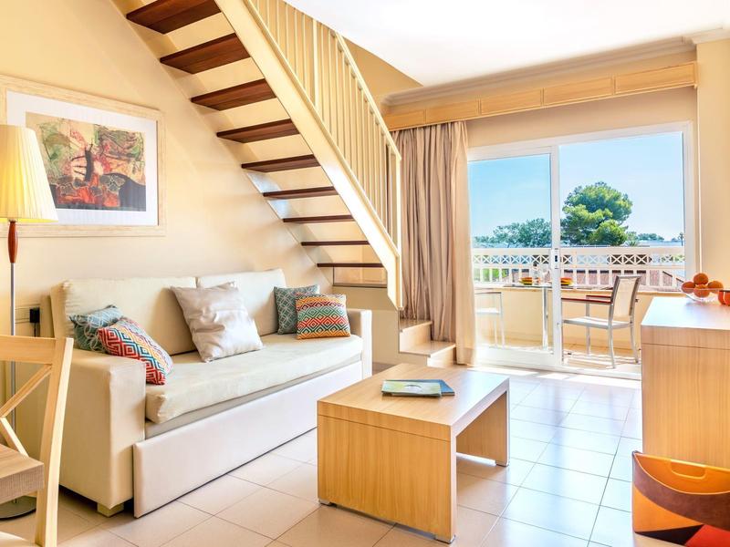 Helles Wohnzimmer mit Sofa, Holztreppe und Zugang zu Balkon mit Blick auf die Natur.