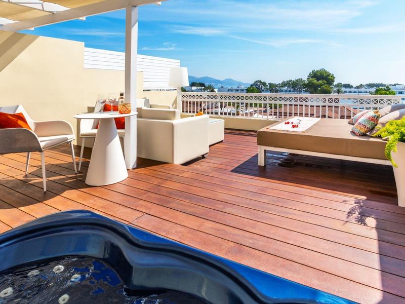 Moderne Dachterrasse mit Whirlpool, Liegestuhl und Sitzbereich mit Blick auf die Berge bei klarem Himmel.