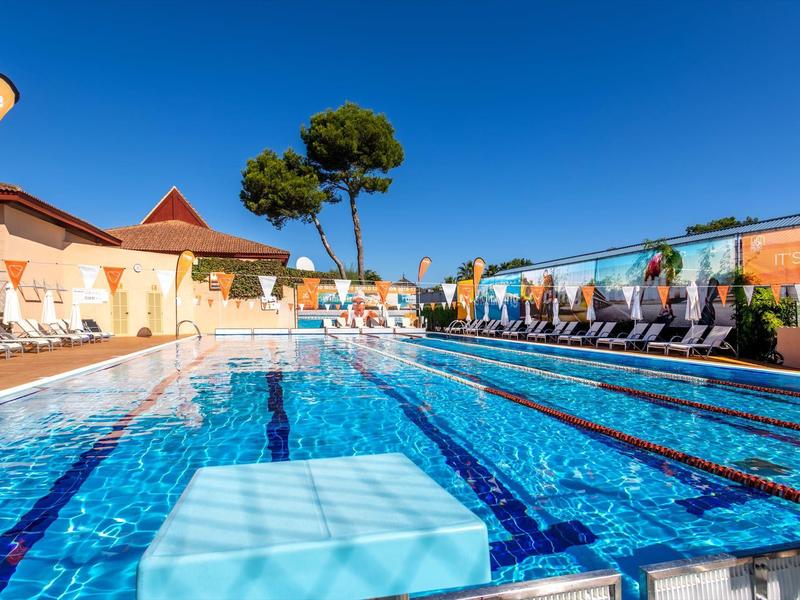Freiluft-Schwimmbad mit Liegestühlen unter klarem blauem Himmel in einem Hotel.