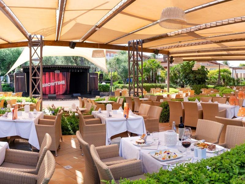 Überdachtes, offen gestaltetes Restaurant mit gedeckten Tischen und Stühlen in hellen Farben.