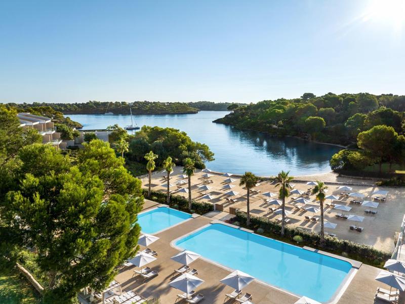 Widok na basen z leżakami z widokiem na spokojne morze z drzewami wzdłuż brzegu.