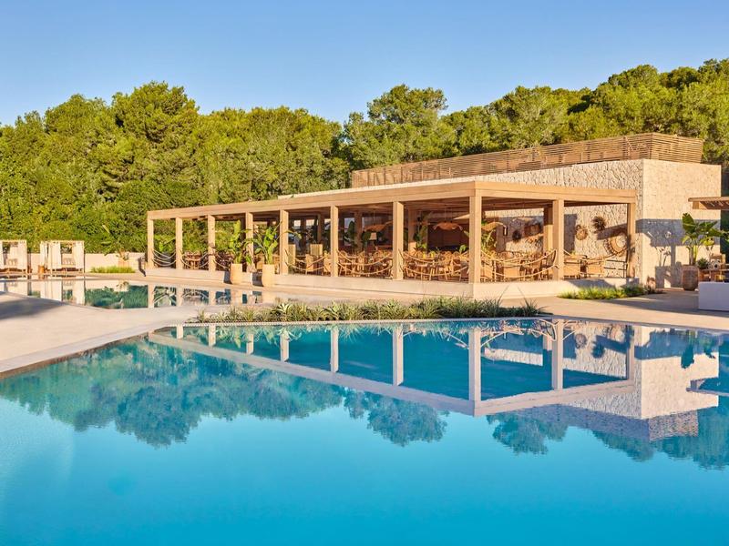 Nowoczesny pawilon z dużymi przeszklonymi oknami obok czystego niebieskiego basenu otoczonego drzewami.