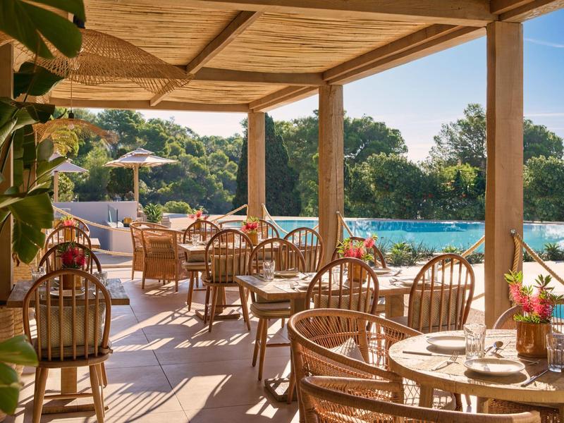 Taras z wiklinowymi krzesłami i stołami obok basenu otoczonego drzewami.