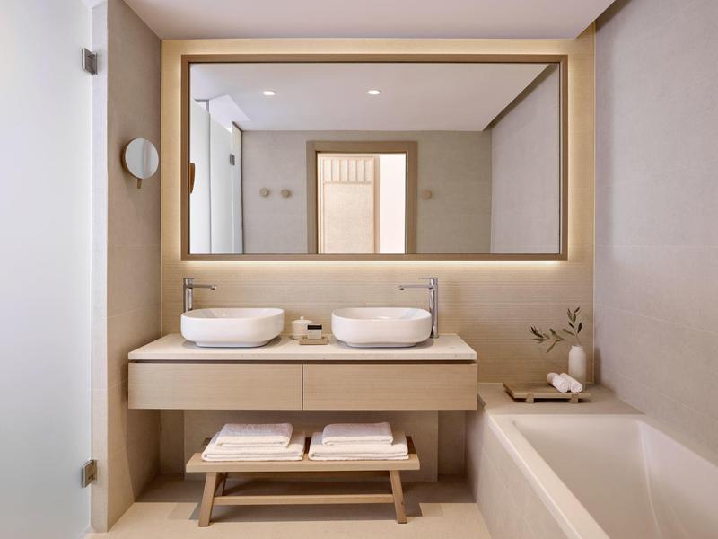 Nowoczesna łazienka z podwójną umywalką, dużym lustrem i wanną w neutralnych kolorach.