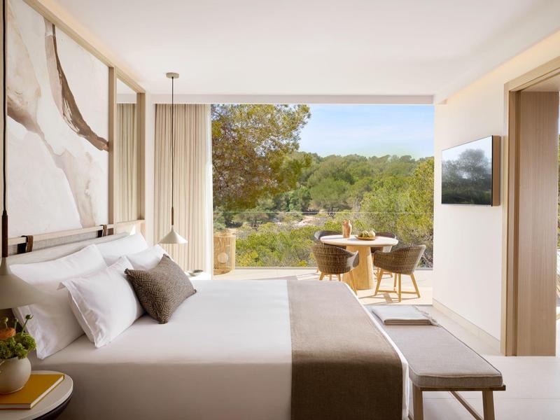 Nowoczesny pokój hotelowy z dużym łóżkiem i widokiem na zielony taras z miejscem do siedzenia.