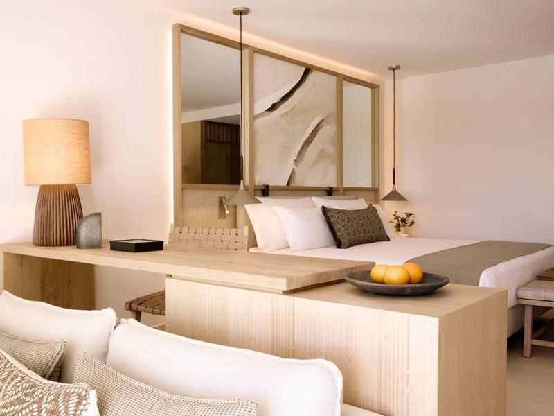 Nowoczesny pokój hotelowy z drewnianymi meblami, białymi ścianami i przytulnym oświetleniem.