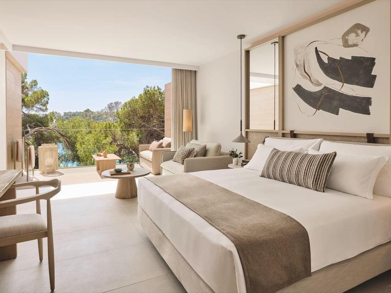 Nowoczesny pokój hotelowy z łóżkiem podwójnym, częścią wypoczynkową i tarasem z widokiem na ogród.